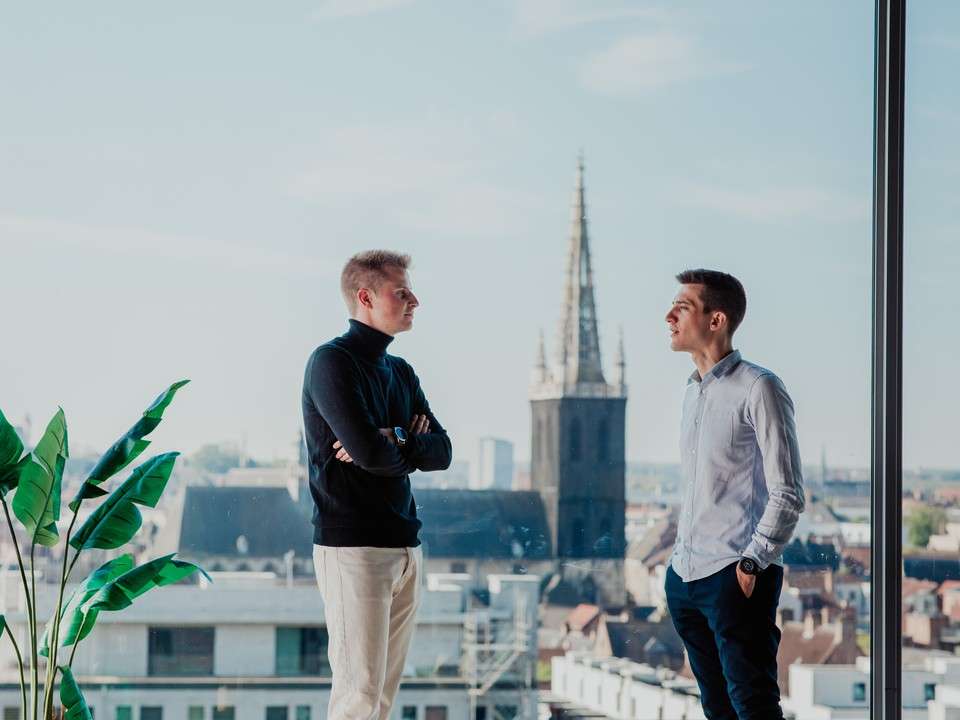 Kristof Borgions and Lars Cappelle talking at a window with the city of Leuven behind them